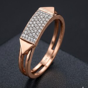 May include: Rose gold ring with a rectangular center encrusted with small, sparkling diamonds. The ring features a double band design and triangular accents on each side of the diamond setting. The inscription "18K 750" is visible on the band.