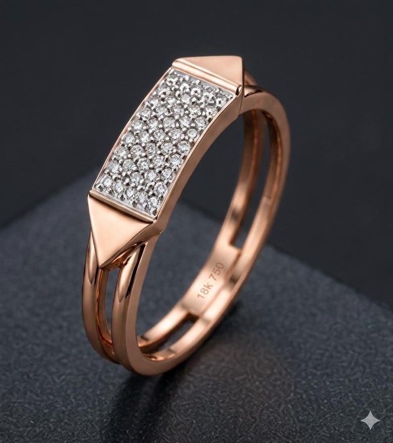 May include: Rose gold ring with a rectangular center encrusted with small, sparkling diamonds. The ring features a double band design and triangular accents on each side of the diamond setting. The inscription "18K 750" is visible on the band.