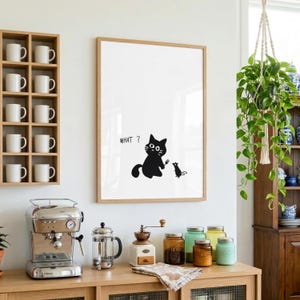 Peut inclure: Un cadre avec une illustration d'un chat noir et d'une souris, avec le mot « WHAT ? » au-dessus du chat. L'œuvre est accrochée sur un mur blanc, au-dessus d'un comptoir en bois avec du matériel à café et des bocaux.