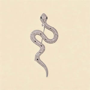 Può includere: Una spilla a forma di serpente color argento con un corpo curvo a forma di S, interamente incastonato con piccole pietre chiare e scintillanti. La testa del serpente presenta due occhi scuri ovali e una spilla metallica sul retro.
