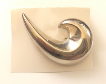 May include: A silver abstract wave-shaped brooch. The brooch is smooth and shiny.