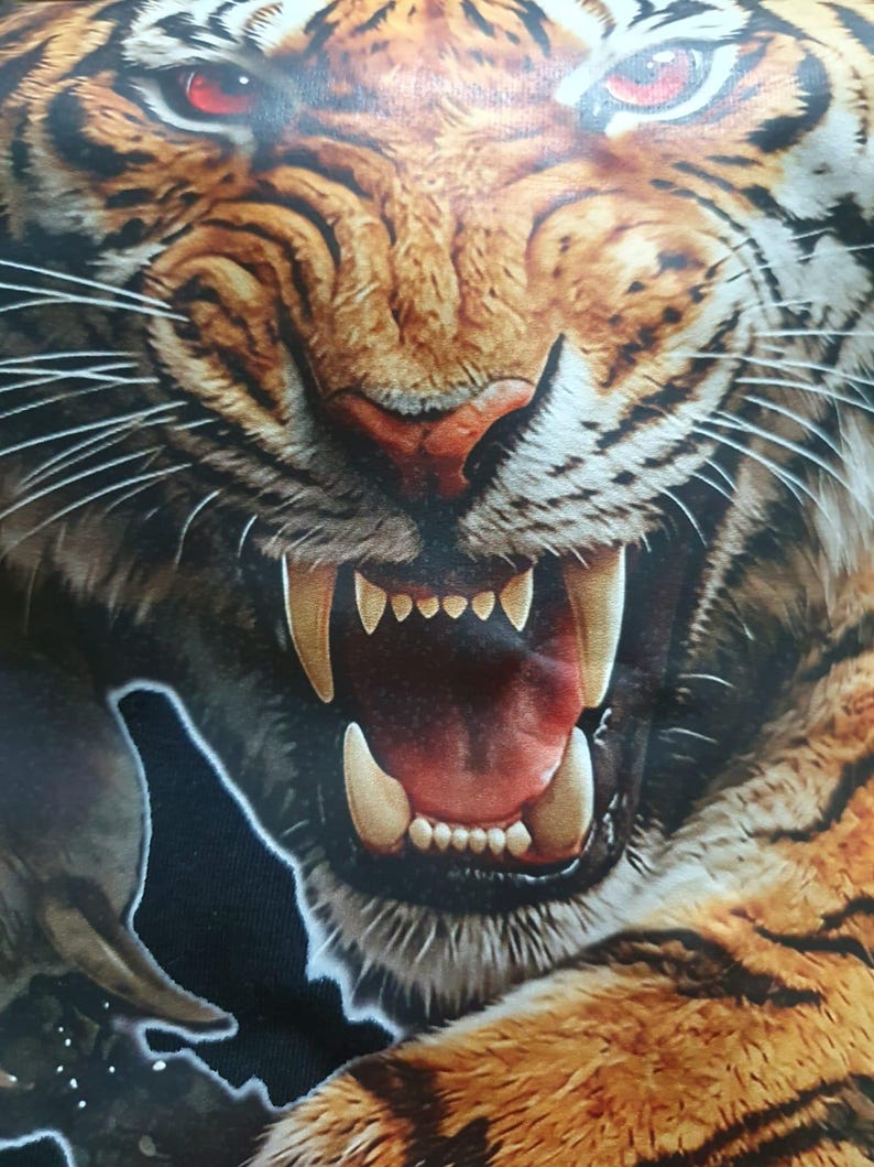 May include: A graphic print of a tiger face with orange, black, and white fur, featuring intense red eyes and an open mouth displaying sharp white fangs and teeth. The tiger is shown in a snarling expression with visible whiskers and detailed fur texture.