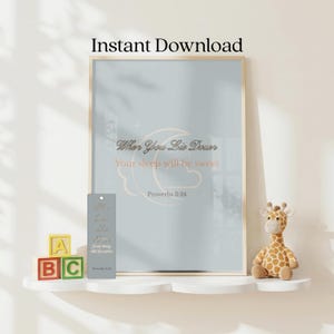 以下が含まれることがあります： 水色の背景に三日月、雲、そして「When You Lie Down Your sleep will be sweet Proverbs 3:24」という文字が描かれた額入りウォールアート。横にはお揃いのブックマークと小さなキリンのぬいぐるみが置かれています。