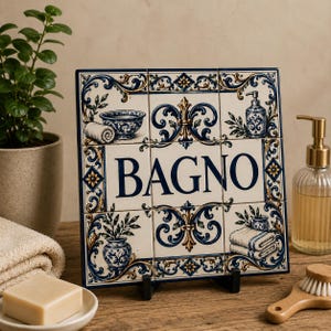 May include: A square decorative tile display featuring nine individual tiles arranged in a grid. The tiles are white with blue and gold ornate scrollwork patterns. The centre tiles feature the word BAGNO in large blue capital letters.