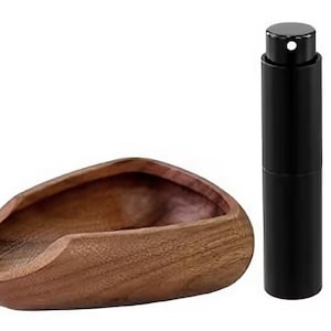Könnte beinhalten: Eine holzfarbene, bootsförmige Schale mit glattem, geschwungenem Design. Daneben befindet sich ein schwarzer, zylindrischer Parfümzerstäuber. Die Schale besteht aus dunkelbraunem Holz, der Zerstäuber hat ein glänzendes, metallisches Finish.