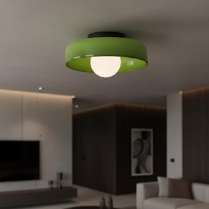 Może przedstawiać: Nowoczesna lampa sufitowa z jasnozielonym kloszem i czarną podstawą. Lampa ma okrągłą, białą żarówkę, która emituje miękką poświatę. Oprawa jest zamontowana na białym suficie w nowoczesnej przestrzeni mieszkalnej.