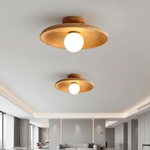 Könnte beinhalten: Zwei Deckenleuchten aus Holz mit natürlicher Holzoberfläche und einer kugelförmigen weißen Glühbirne. Die Leuchten sind an einer weißen Decke in einem modernen Wohnraum montiert. Das Design ist minimalistisch und modern.