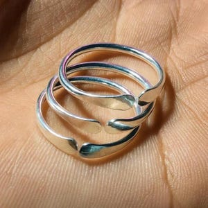 Könnte beinhalten: Drei silberfarbene, verstellbare Zehenringe sind gestapelt. Die Ringe haben ein einfaches, offenes Design mit glatter, reflektierender Oberfläche. Die Ringe sind aus glänzendem Metall. Sie liegen auf einer hellbraunen Oberfläche.