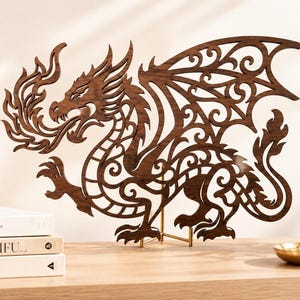 Peut inclure: Une sculpture de dragon en bois brun foncé découpée au laser avec des motifs en filigrane complexes, représentée de profil avec les ailes déployées et des flammes sortant de la gueule, sur un support en métal doré fin sur une surface plane.