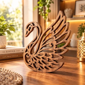 May include: A brown wooden swan sculpture featuring intricate laser-cut filigree patterns throughout its body and wings. The swan is depicted in a side profile with its neck curved and wings extended upward, showcasing a detailed openwork design.