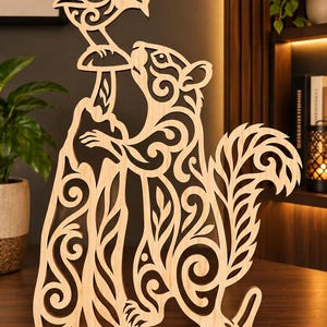 May include: A light-colored wooden cutout sculpture featuring a squirrel standing on its hind legs next to a tree trunk, holding a mushroom. A small bird is perched atop the mushroom. The entire piece displays intricate, swirling cut-out patterns.