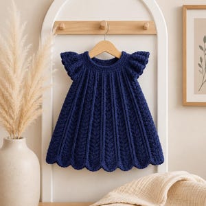 Può includere: Un abito all'uncinetto blu navy scuro con scollo rotondo, maniche corte a volant e un motivo a coste verticali che si estende fino a un orlo smerlato. Il capo è esposto su una gruccia di legno, mettendo in risalto la lavorazione a maglia.