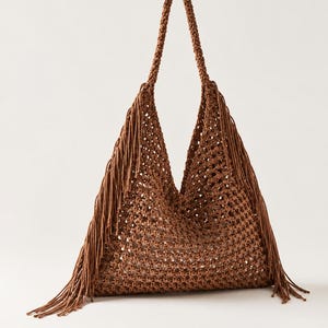 May include: A brown macrame shoulder bag featuring an open-weave knotted pattern, a single braided handle, and long fringe detailing along the side edges. The bag has a triangular silhouette and is constructed from a textured cord material.