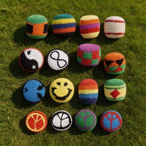 Puede incluir: Una colección de coloridas pelotas de malabares de ganchillo dispuestas sobre hierba verde. Las pelotas presentan varios diseños, incluyendo rayas, patrones geométricos y símbolos como un yin-yang, una bola ocho y una carita sonriente. La paleta de colores incluye tonos vibrantes de rojo, naranja, amarillo, verde, azul y morado.