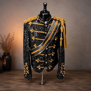 Peut inclure: Veste noire à sequins avec des détails dorés, présentée sur un mannequin. La veste comporte des épaulettes, des boutons et une ceinture dorés. Le design rappelle un uniforme militaire, avec un col haut et des détails complexes. Une pièce de mode audacieuse.