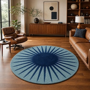 May include: A large circular area rug featuring a deep navy blue center with radiating sunburst rays in alternating shades of light blue and dark blue, creating a bold geometric pattern that covers the entire surface of the round floor covering.