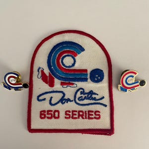 Könnte beinhalten: Ein weißes Patch mit rotem Rand mit dem Text "Don Carter 650 SERIES" in blauer Schrift. Das Patch hat ein Bowlingkugel-Design in Rot, Weiß und Blau. Zwei Anstecknadeln mit einem Bowlingkugel-Design und den Zahlen "275" und "225" sind ebenfalls vorhanden.