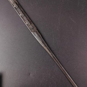 May include: A silver hairpin with a floral design. The hairpin has three sets of flowers along its length and a small hook at the top. The metal has a slightly aged appearance.