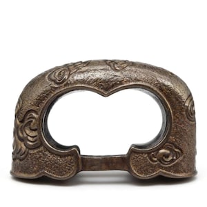 May include: A bronze-colored, decorative metal lock with an arched top and a heart-shaped opening. The lock features intricate floral and cloud-like patterns on its surface. The design is symmetrical and has a vintage aesthetic.