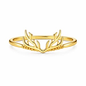 Könnte beinhalten: Ein goldfarbener Ring mit einem stilisierten Hirschgeweih-Design. Der Ring hat ein glattes, poliertes Band und die Geweihe sind aufwendig detailliert. Der Ring ist vor einem weißen Hintergrund platziert, was sein elegantes Design hervorhebt.