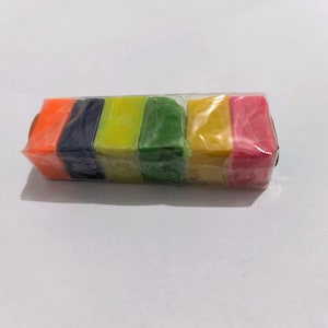 May include: A rectangular block of modeling clay wrapped in clear plastic, featuring six distinct segments in vibrant colors including orange, dark blue, lime green, forest green, yellow, and pink, arranged side by side in a single row.