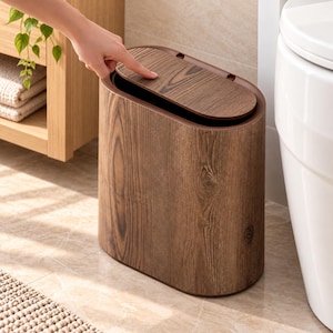 May include: An oval-shaped waste bin featuring a dark brown wood grain finish. The container has a hinged lid that opens with a push mechanism, revealing a dark interior. The exterior surface displays a realistic wood texture pattern throughout.