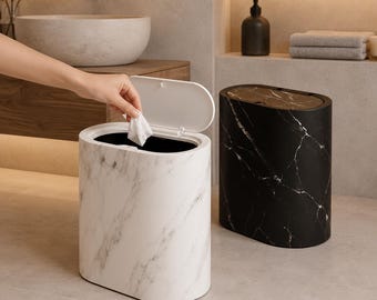 May include: Two oval-shaped waste bins with a marble pattern. One bin is white with grey veining and features an open lid, while the other is black with white veining and a closed lid. Both containers have a smooth finish and a modern, sleek design.