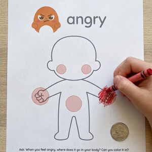 Könnte beinhalten: Ein weißes Blatt Papier mit dem Wort "angry" und einer Cartoon-Illustration eines wütenden Gesichts. Ein Kind malt die Illustration mit einem roten Buntstift aus. Eine 2,5 cm Münze befindet sich neben der Illustration. Der Text "Ask: When you feel angry, where does it go in your body?" steht unten.
