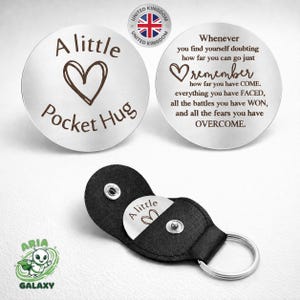 May include: Two silver pocket hug tokens with inspirational messages. One has a heart and the words "A little Pocket Hug." The other says "Remember how far you have come." A black leather keychain case holds one token.