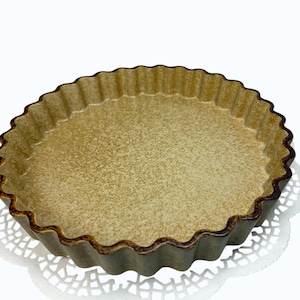 Puede incluir: Un molde redondo de cerámica para tartas con borde ondulado y acabado moteado en tonos beige y marrón. La superficie interior presenta un aspecto texturizado con tonos marrones más oscuros concentrados a lo largo del borde festoneado.