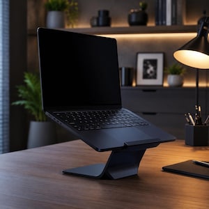 May include: A black laptop computer is elevated on a sleek, curved black stand. The laptop's screen is dark, and the keyboard is visible. The stand is on a wooden desk, with a lamp and office supplies in the background.