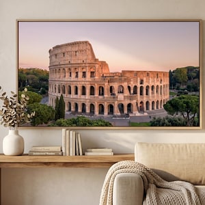 Puede incluir: Una impresión enmarcada del Coliseo en Roma, Italia, al atardecer. El antiguo anfiteatro es el punto focal, con su estructura arqueada y la vegetación circundante. La impresión se exhibe sobre una consola de madera.