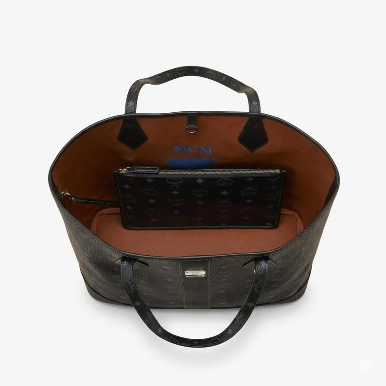 Puede incluir: Bolso tote negro con una bolsa negra a juego en el interior. El bolso tote tiene un patr&oacute;n texturizado y dos asas. El interior es marr&oacute;n con texto azul. La bolsa tiene cierre de cremallera y un patr&oacute;n repetitivo.