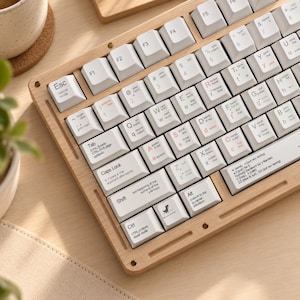 May include: A mechanical keyboard with a light wood frame and white keycaps. The keys feature black text detailing various computer commands and shortcuts, including specific Vim editor functions. A small dinosaur icon is printed on one key.