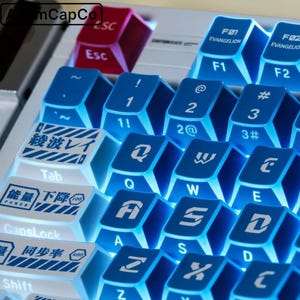 May include: Close-up of a mechanical keyboard with custom keycaps. The keycaps are primarily blue and white, with Japanese characters and English letters. The "Esc" key is red. The keyboard is lit with a blue backlight, enhancing the visibility of the key legends.