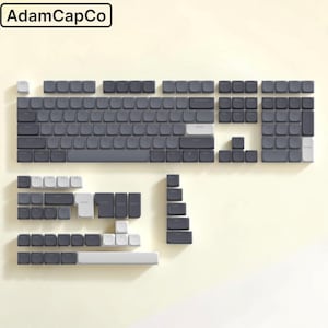 Puede incluir: Un juego completo de teclas para teclado mecánico en gris oscuro y gris claro dispuestas en una distribución estándar. El conjunto incluye teclas alfanuméricas, teclas de función, un teclado numérico y teclas modificadoras.
