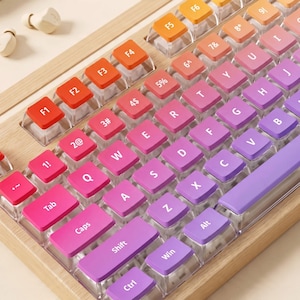 May include: A mechanical keyboard with a light wood frame and a gradient colour scheme on the keycaps, transitioning from orange and red at the top left to pink, purple, and violet across the QWERTY layout and bottom keys.