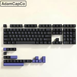May include: A full set of black mechanical keyboard keycaps with purple legends and additional purple accent keys. The layout includes a standard QWERTY arrangement, a numeric keypad, and function keys. The text AdamCapCo is visible in the top left.