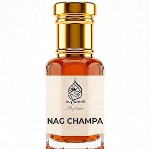May include: A clear glass perfume bottle with a gold-colored cap, filled with an amber-colored liquid. The white label features a black logo, the text Al Kumar Perfume, and the bold black text NAG CHAMPA centered on the front of the bottle.