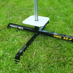 May include: A black metal target stand with a white square base. The stand has a black metal pole with the text "KNIGHT MFG" and a black metal arm with the text "TARC 32-F".