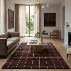 Pode incluir: Um tapete retangular com uma base castanho-escura e um padrão de grelha composto por linhas finas cor-de-rosa claro. O tapete está colocado sobre um chão de madeira clara numa sala com um sofá, uma mesa de centro e um candeeiro moderno.