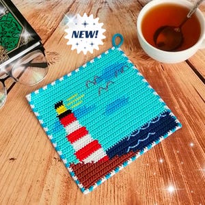 May include: A square, turquoise potholder with a lighthouse design. The lighthouse is red and white with a black and yellow top. The potholder has a blue loop for hanging and the word "NEW!" in a white starburst.
