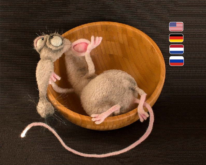 Pode incluir: Um brinquedo de rato de malha cinza e rosa com olhos grandes, sentado em uma tigela de madeira. O rato tem uma cauda longa que est&aacute; enrolada ao redor da tigela.
