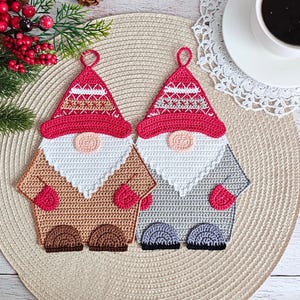 Puede incluir: Dos salvamanteles hechos a mano en ganchillo con forma de gnomo. Uno es de color beige con un gorro rojo, barba blanca y nariz rosa. El otro es gris con un gorro rojo, barba blanca y nariz rosa. Ambos tienen pies marrones o morados y mitones rojos.
