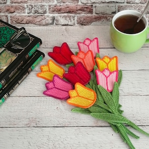 Könnte beinhalten: Ein Strauß gehäkelter Tulpen in Rot-, Orange-, Gelb-, Rosa- und Grüntönen. Die Tulpen sind fächerförmig angeordnet, wobei die Stiele nach rechts verlaufen.