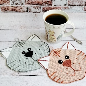 May include: Two crocheted cat-shaped pot holders. One is gray with black eyes and nose, the other is tan with brown eyes and nose.