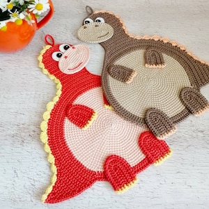 May include: Two crocheted dinosaur-shaped pot holders. One is red with yellow accents and the other is brown with beige accents.