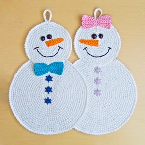 May include: Two crocheted snowman pot holders, one with a blue bow and the other with a pink bow. Both have orange noses and black eyes.