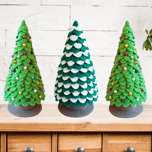 May include: Three crocheted Christmas trees, one green with colorful beads, one green and white with white beads, and one green with colorful beads. The trees are on a wooden shelf with drawers.