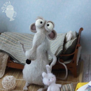 Pode incluir: Um rato de croch&ecirc; cinza com olhos grandes e uma cauda longa est&aacute; ao lado de um coelho de croch&ecirc; branco. O rato est&aacute; com o bra&ccedil;o direito levantado no ar. O coelho est&aacute; sentado em um tapete listrado.